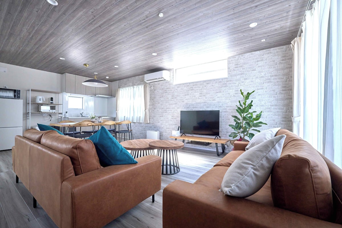 Een moderne woonkamer met een bruine leren bank, een televisie, en een eethoek met een houten tafel en stoelen.