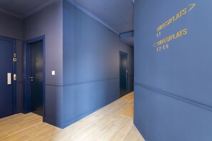 Un pasillo con paredes azules y suelo de madera, que conduce a puertas con números de habitación.