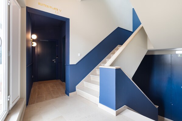 Una escalera moderna con detalles azules y blancos que conduce a una puerta con la leyenda 'Suites/Flats V 1.1'.