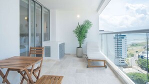Un balcón con mesa y sillas de madera, una planta en maceta y una silla blanca acolchada.