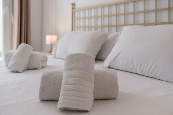 A neatly made bed with white linens and rolled towels.