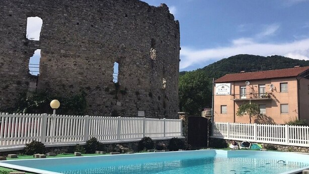 Une piscine avec un mur en pierre et une clôture blanche au premier plan, et un bâtiment avec une enseigne en arrière-plan.