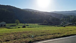 Un paysage rural avec une route, des granges et des collines douces sous un ciel dégagé.