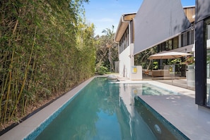Uma área de piscina moderna ao ar livre, com cercado de bambu, piscina cristalina e um edifício contemporâneo com amplas janelas e área de estar externa.