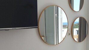 Ein Zimmer mit einem Flachbildfernseher, drei runden Spiegeln, einem Holzstuhl und einem kleinen runden Tisch mit einer Katze.