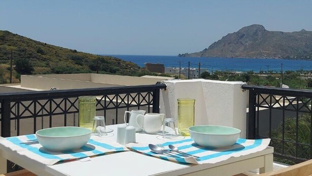 Eine Terrasse mit gedecktem Tisch für zwei Personen, mit Blick auf eine Küstenlandschaft mit Hügeln und dem Meer.