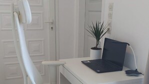 Ein weißer Schreibtisch mit einem Laptop, einer Topfpflanze und einem weißen Bürostuhl in einem Raum mit weißen Wänden und Fliesenboden.