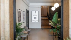Un pasillo con obras de arte enmarcadas, una escalera y plantas en macetas.