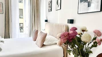 A hotel room with a bed, a bedside table, a vase of flowers, and artwork on the wall.