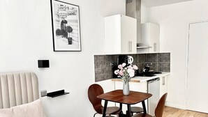 Moderni hotellihuone, jossa on sänky, pieni ruokapöytä tuoleineen, keittiöalue kaappeineen sekä seinällä oleva taulu.