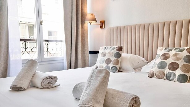 Hotellihuone, jossa on sänky, tyynyjä ja ikkuna, jossa on verhot.