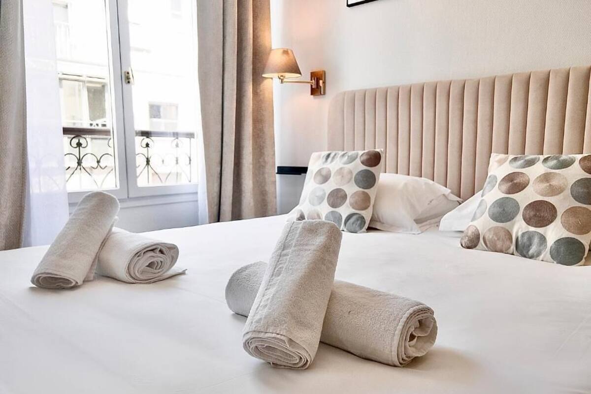 A hotel room with a bed, pillows, and a window with curtains.
