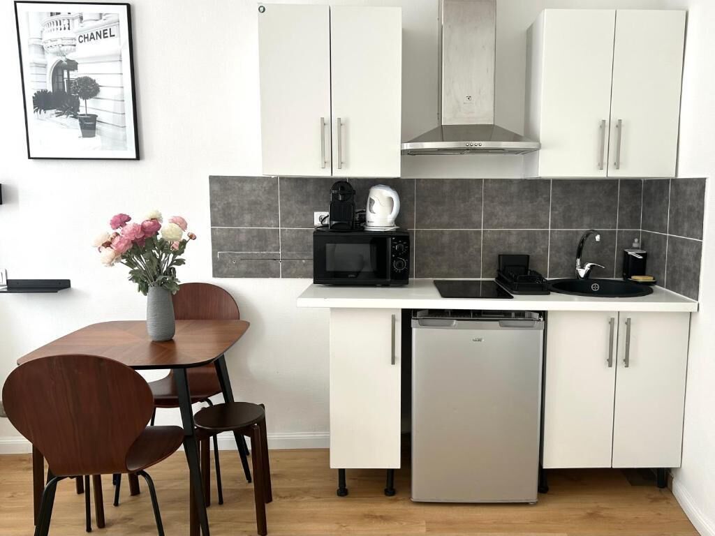 Una cocina compacta con armarios blancos, microondas, cafetera y lavavajillas.