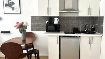 Una cocina compacta con armarios blancos, microondas, cafetera y lavavajillas.