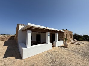 A small, white building with a stone wall backdrop, a covered seating area, and a potted plant. - Renovated farmhouse (Pilar de la Mola)