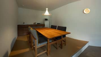 A compact dining area with a wooden table and chairs, a hanging light fixture, and a kitchenette in the background.