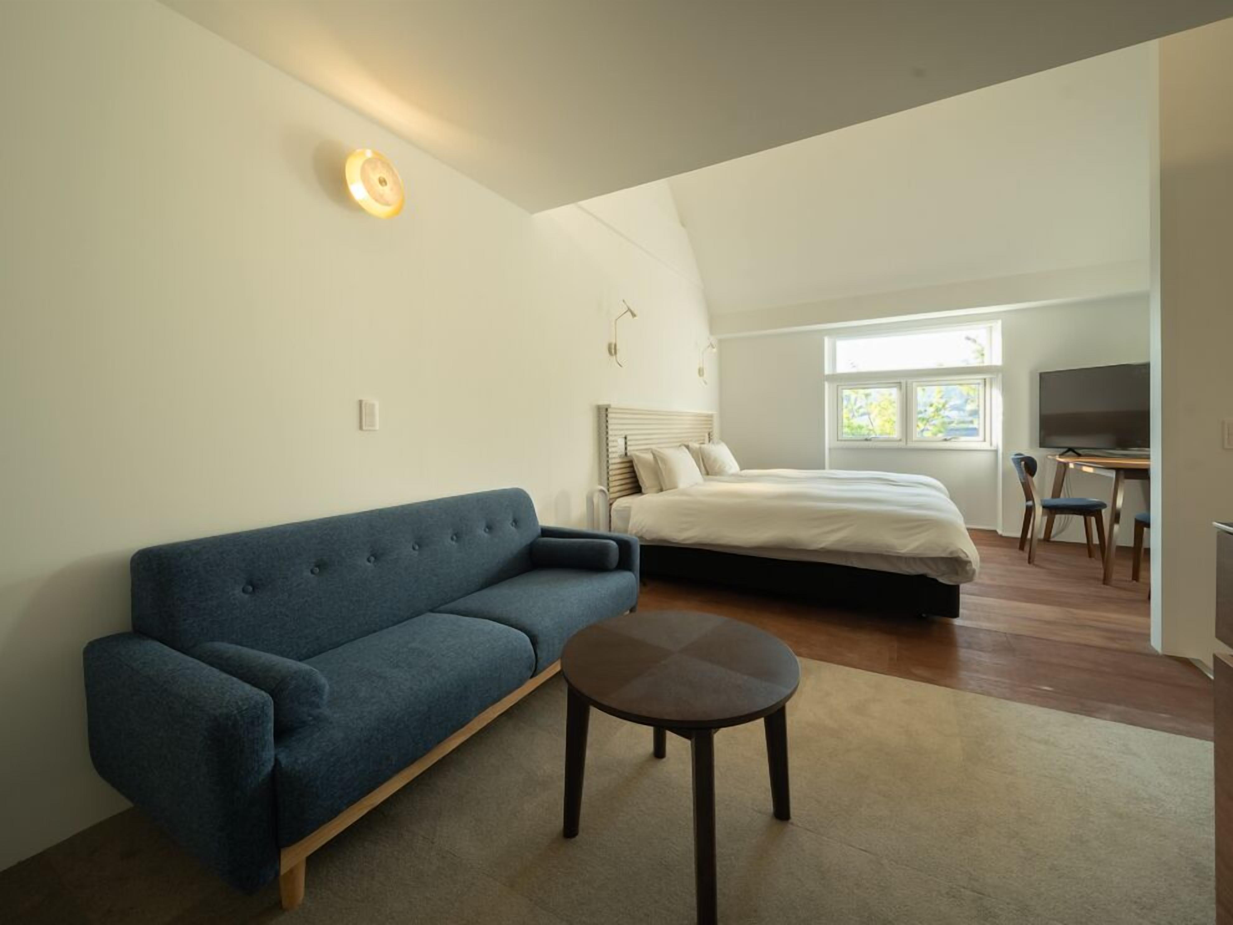 Une chambre à coucher avec un lit, un canapé bleu, une petite table, un téléviseur et une fenêtre.