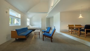 A spacious living room with a high ceiling, a blue sofa, a wooden coffee table, and a dining area with a wooden table and chairs. - Nishi-Karuizawa Hotel atelier bla by LONGINGHOUSE (Miyota)