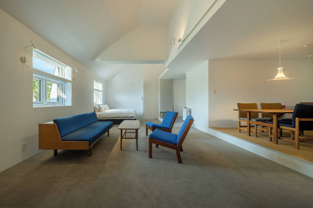 Uma sala de estar ampla com teto alto, um sofá azul, uma mesa de centro de madeira e um espaço de jantar com mesa e cadeiras de madeira.