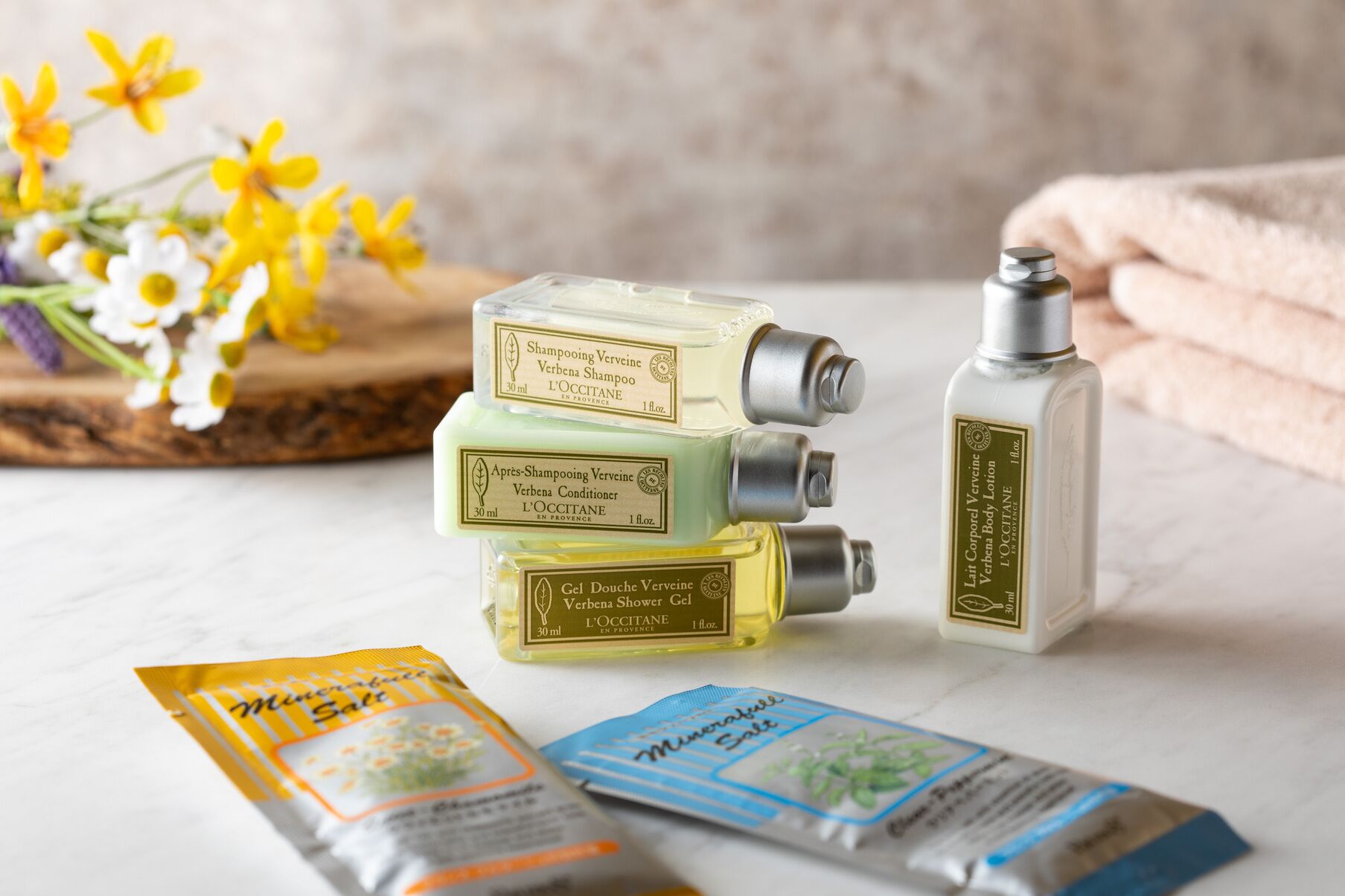 Una colección de productos Verveine de L'OCCITANE que incluye champú, acondicionador, gel de ducha y loción corporal, junto con sobres de sales minerales.