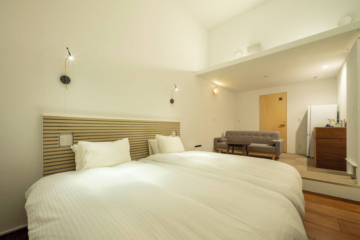 Quarto de hotel com uma cama grande, um sofá, uma pequena mesa e uma área de kitchenette.