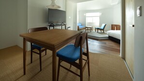 A modern hotel room with a wooden dining table, two blue chairs, a flat-screen TV, a sofa, and a bed. - Nishi-Karuizawa Hotel atelier bla by LONGINGHOUSE (Miyota)