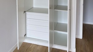 A white walk-in closet with open doors, a hanging light fixture, and a wooden floor.