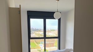 A bedroom with a bed, a large window, and a view of the city.