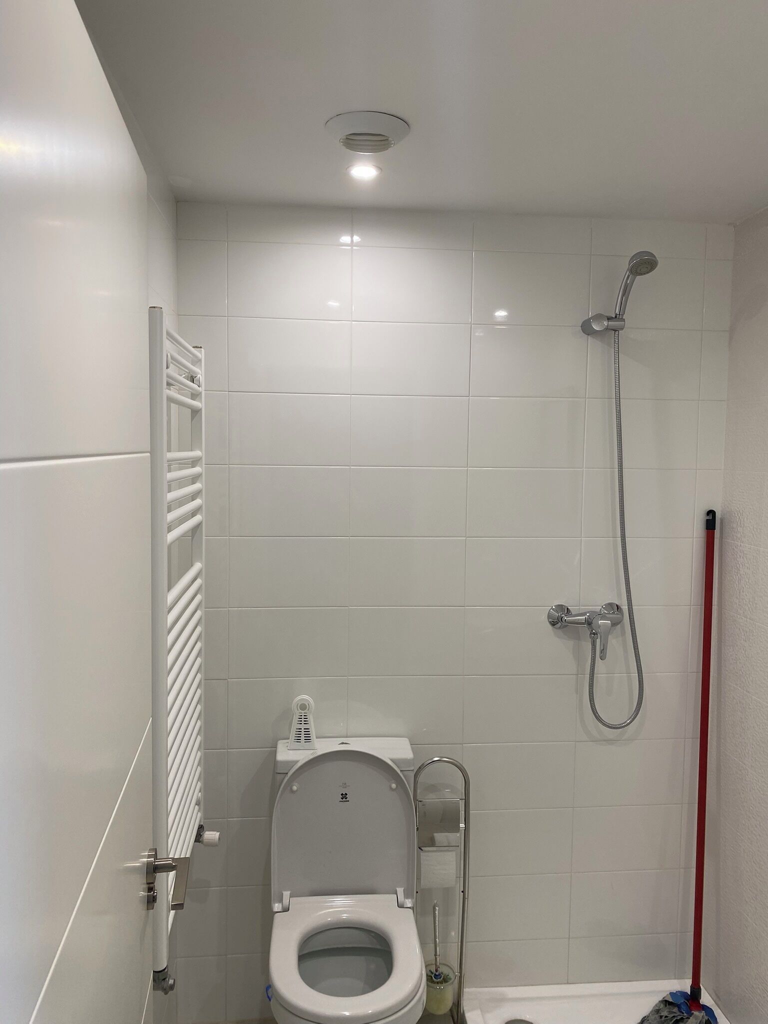 Et lille, moderne badeværelse med hvide fliser, toilet, brusebad og en radiator.