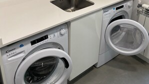 A compact laundry area with a sink, two front-loading washing machines, and a countertop.