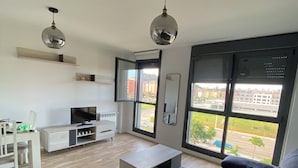 A modern living room with a large window, a TV, a sofa, and a dining area.