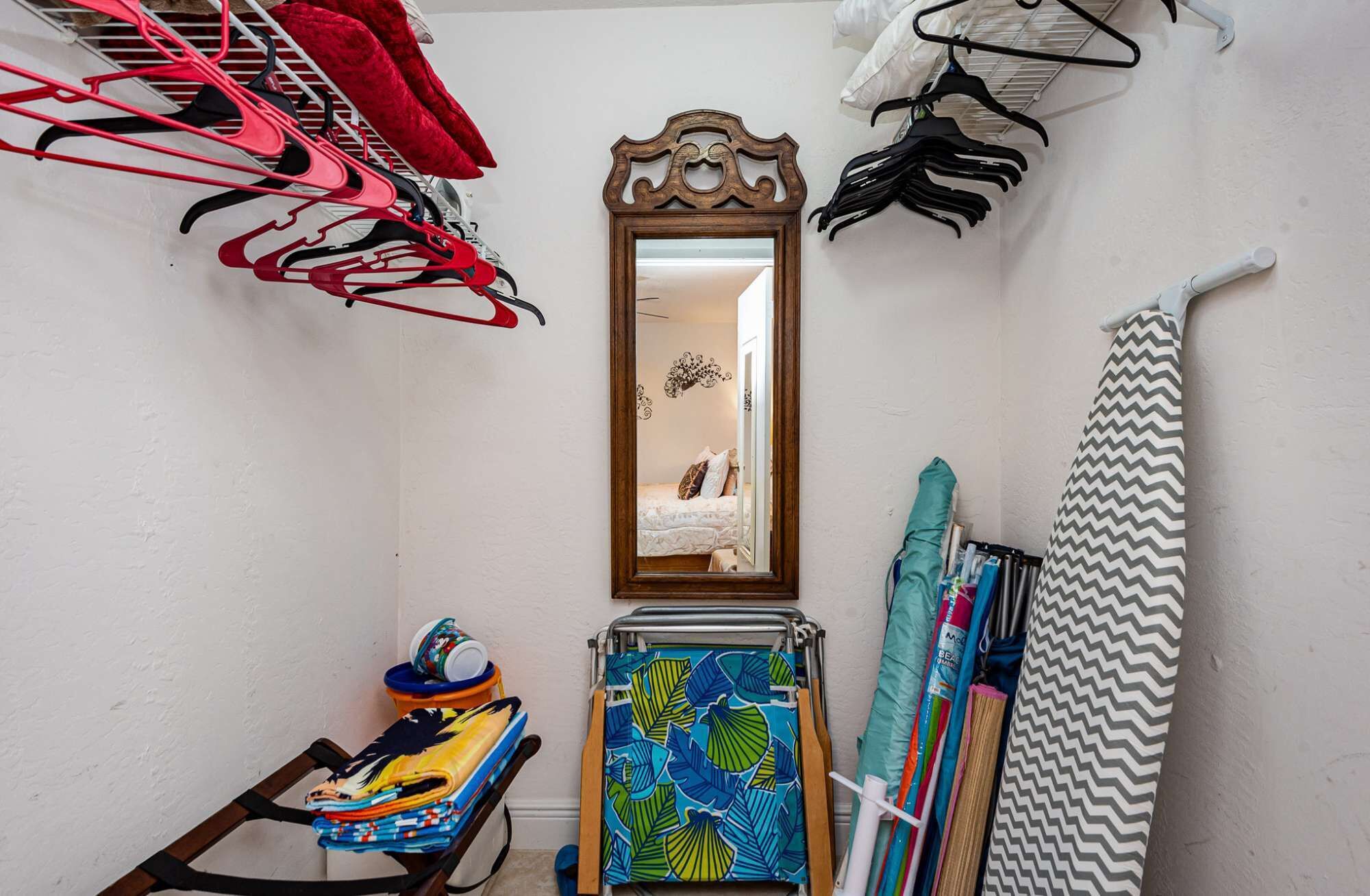 A small, narrow room with a wooden-framed mirror, a folding chair, and a rack of colorful towels.