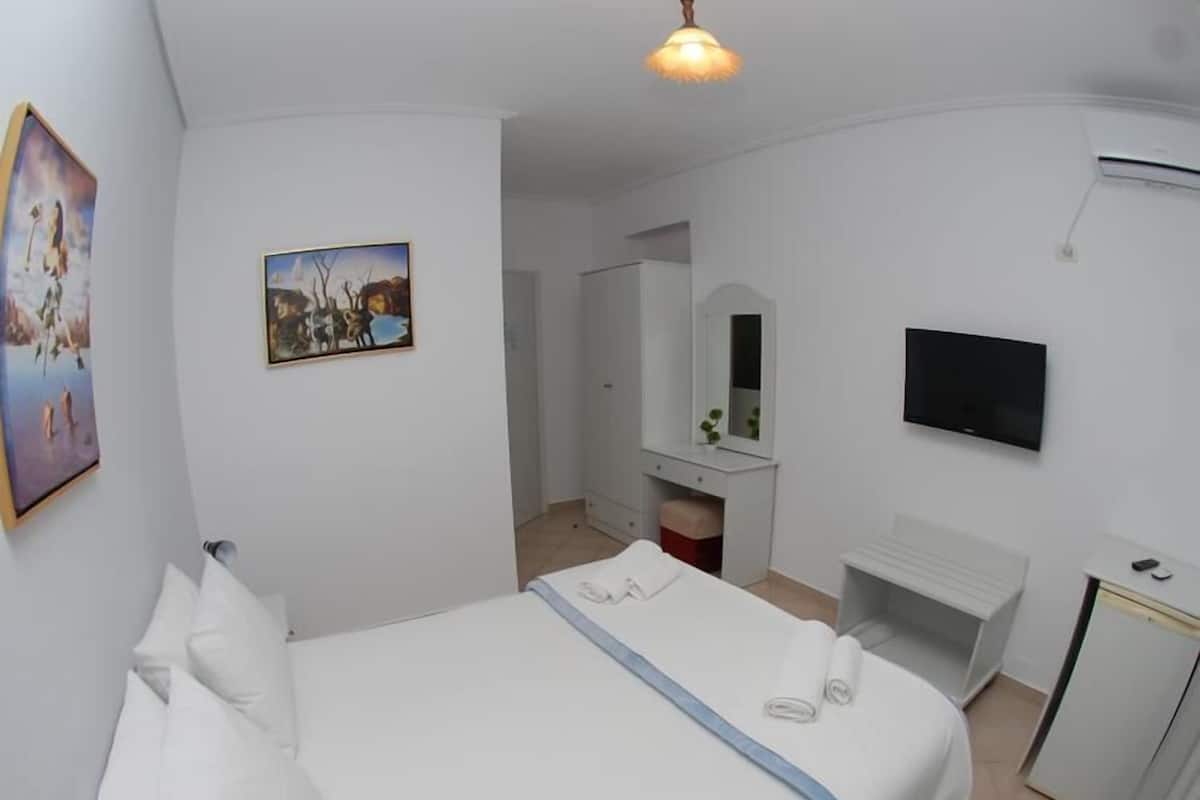 Un dormitorio con una cama grande, televisor, escritorio y espejo.