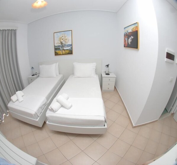 A hotel room with two single beds, a nightstand with a lamp, and two paintings on the walls.