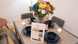 Una mesa de comedor dispuesta con platos azules, un jarrón de flores de colores y un cartel con el menú.