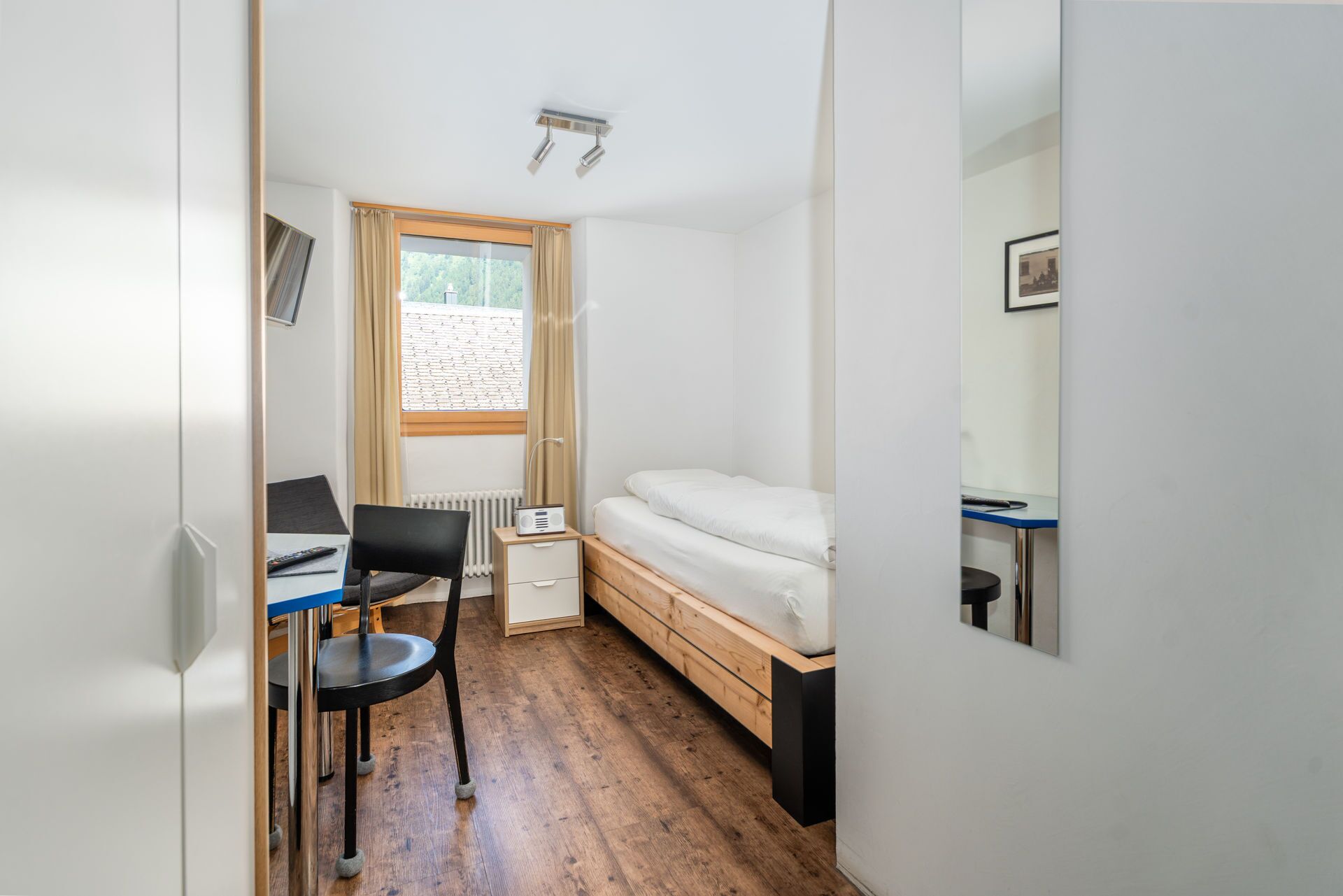 Una habitación pequeña con cama, escritorio, silla y ventana con cortinas.