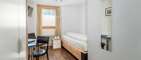 Una habitación pequeña con cama, escritorio, silla y ventana con cortinas.