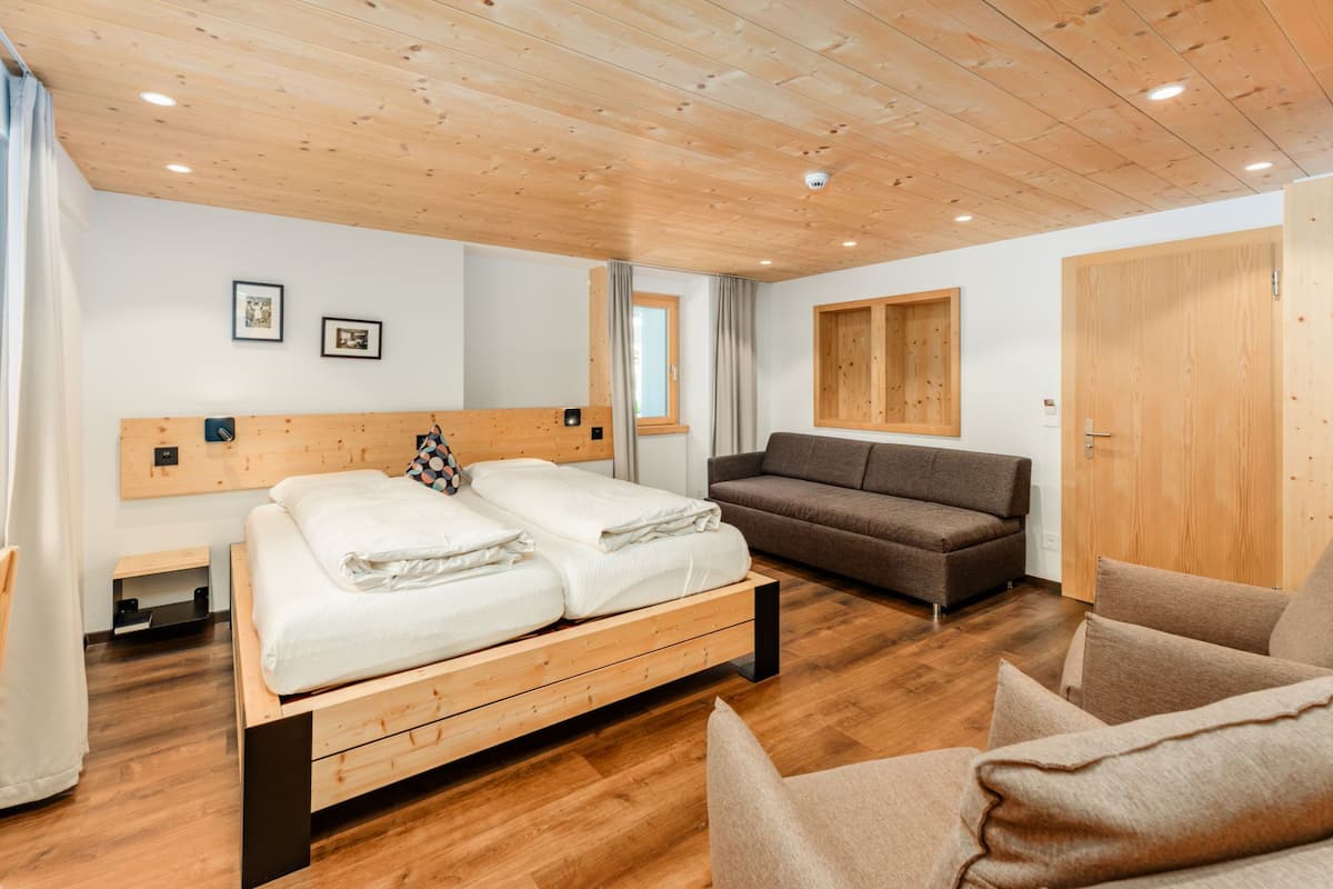 A modern bedroom with a wooden ceiling, a double bed, a sofa, and a wardrobe.