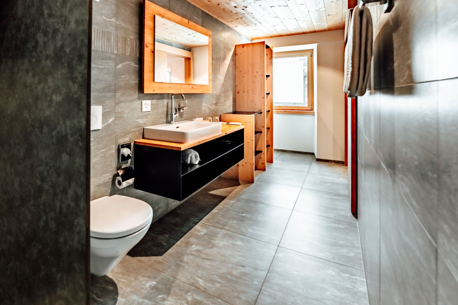A modern bathroom with a wooden vanity, a white toilet, and a large mirror.