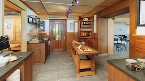 A kitchen with wooden cabinets, a central island, and a dining area with chairs. - Hotel Furka (Obergoms)