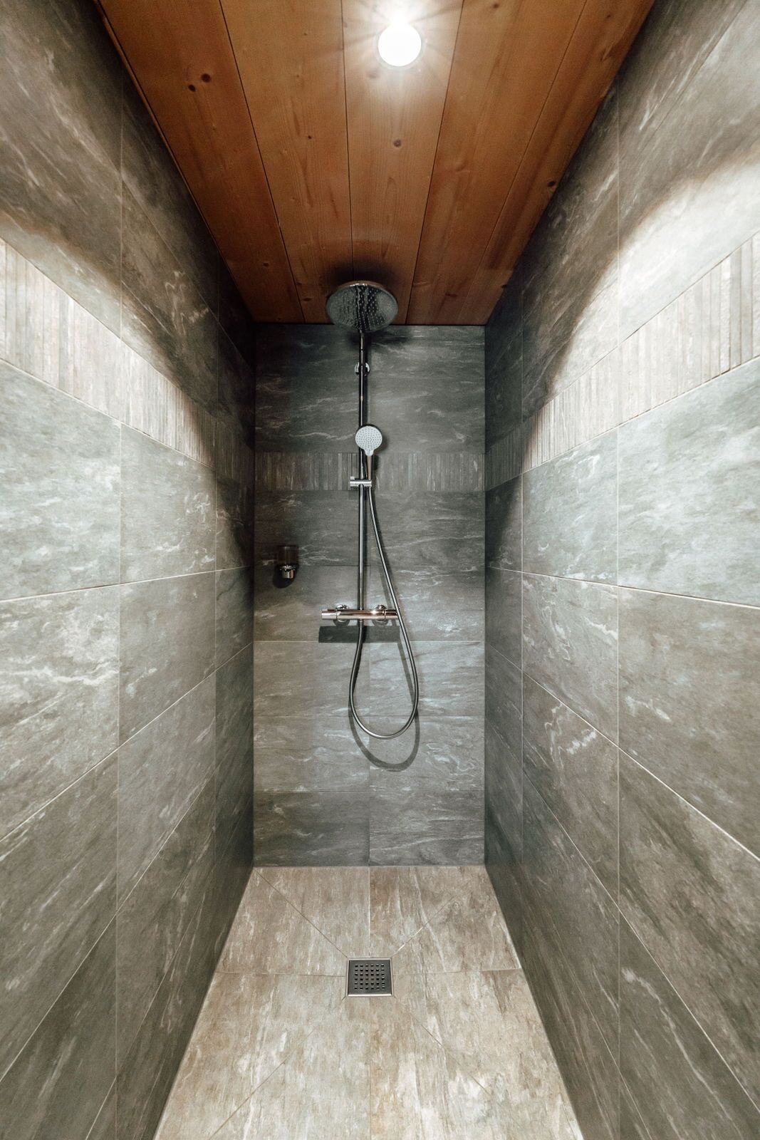 A shower with a wooden ceiling and tiled walls.