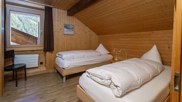 A room with two beds, a chair, a radiator, and a window with a view of trees.
