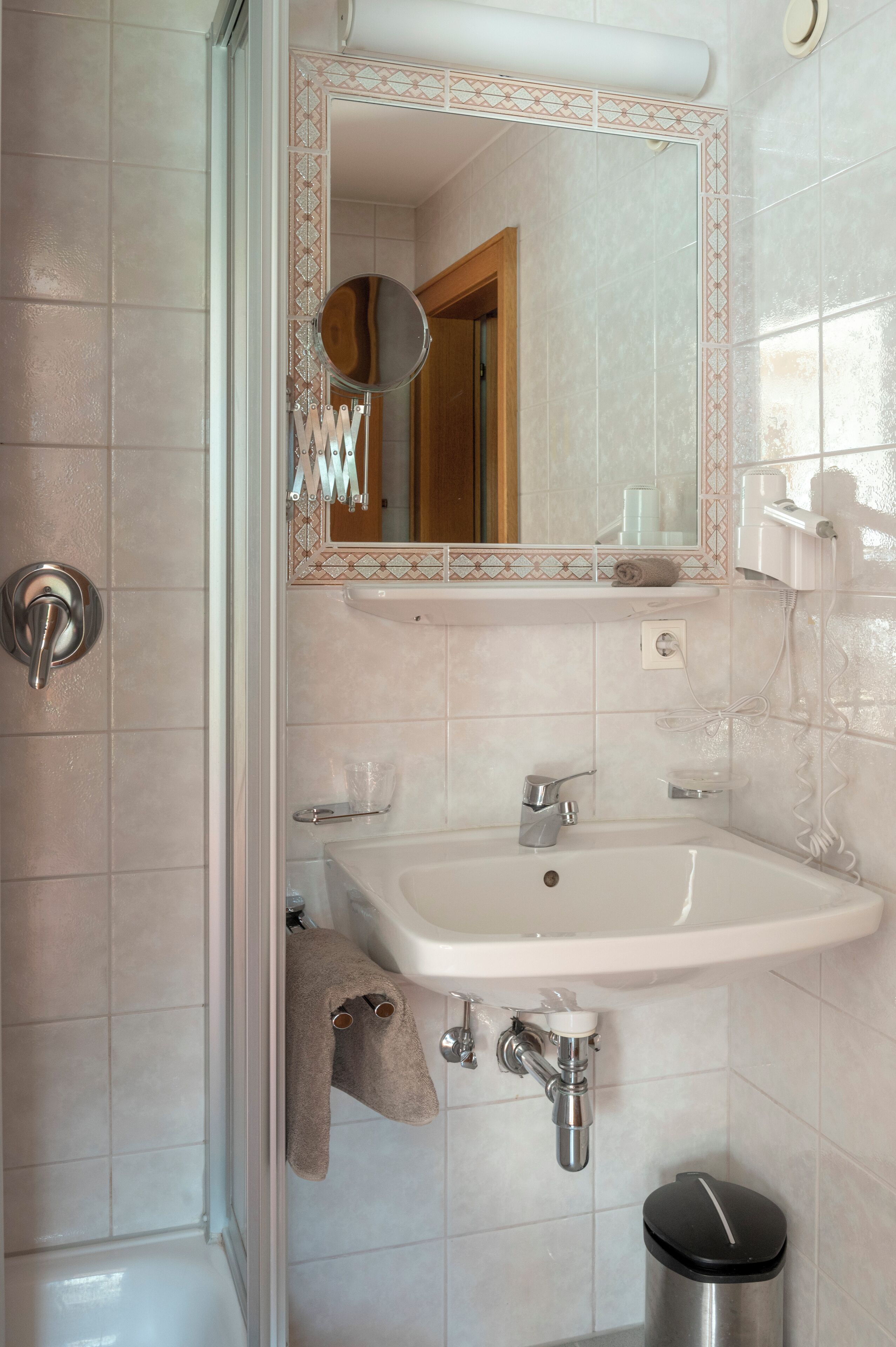 Un baño con lavamanos blanco, espejo, toallero y cubo de basura.