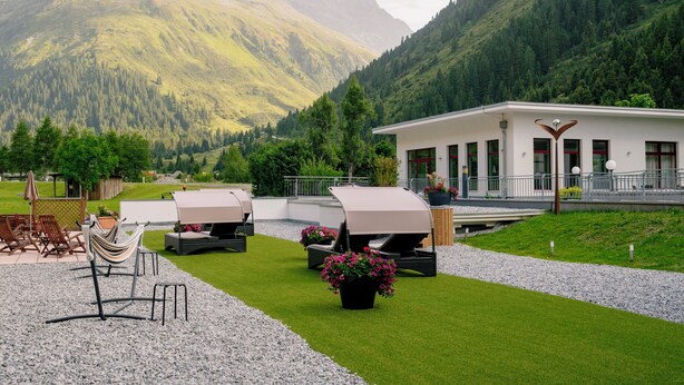 A modern outdoor seating area with a barbecue grill, surrounded by a well-maintained lawn and gravel path, with a mountain backdrop. - Alpine B&B (Sankt Leonhard im Pitztal)