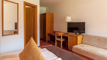 A hotel room with a bed, a sofa, a desk with a chair, a television, and a wardrobe.