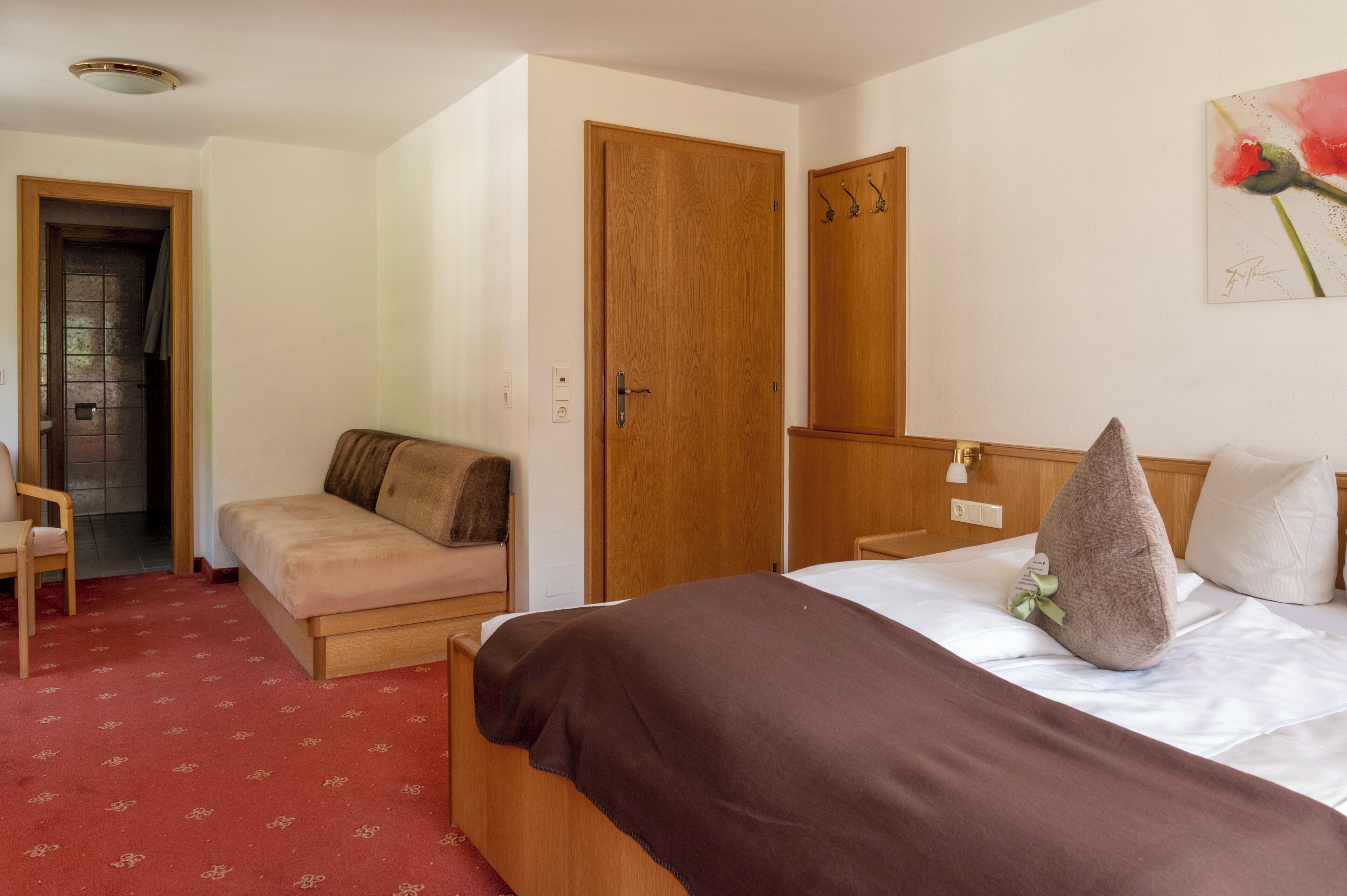 Una camera d'albergo con un letto, un armadio in legno, una poltrona e un quadro appeso al muro.