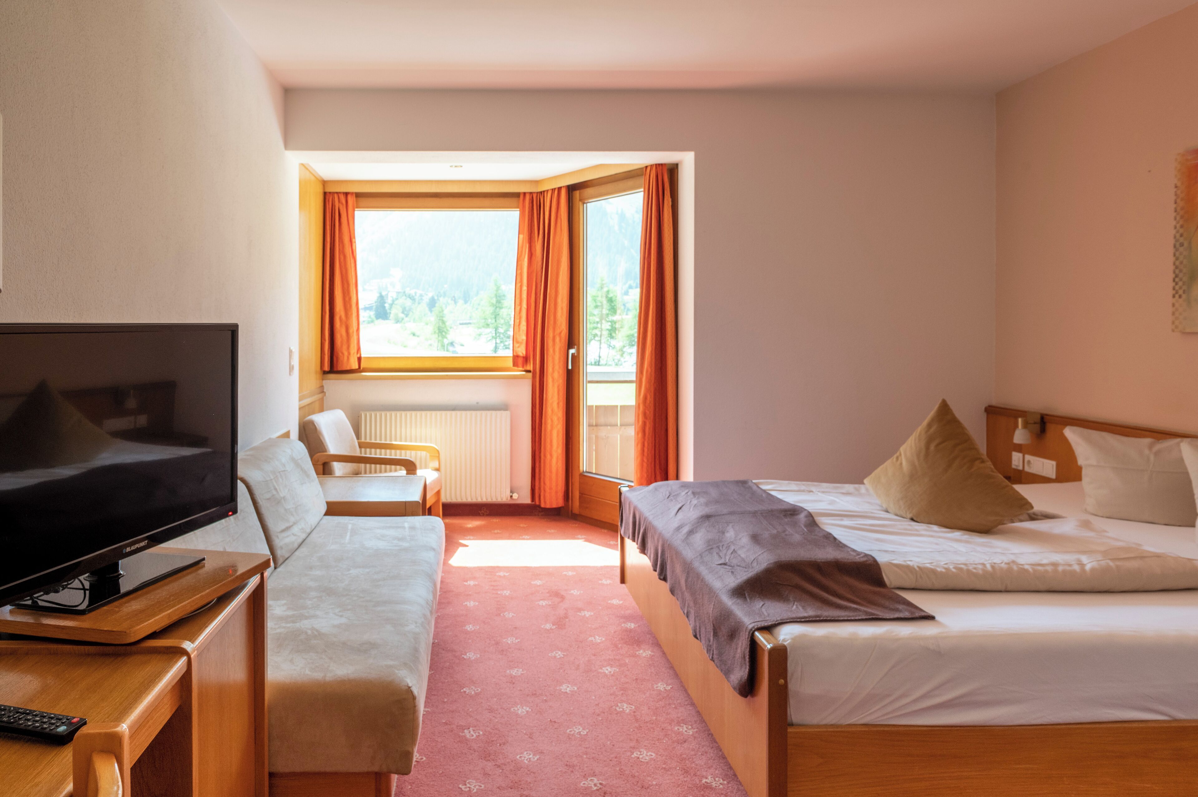 A hotel room with a TV, a sofa, a bed, and a window with curtains.