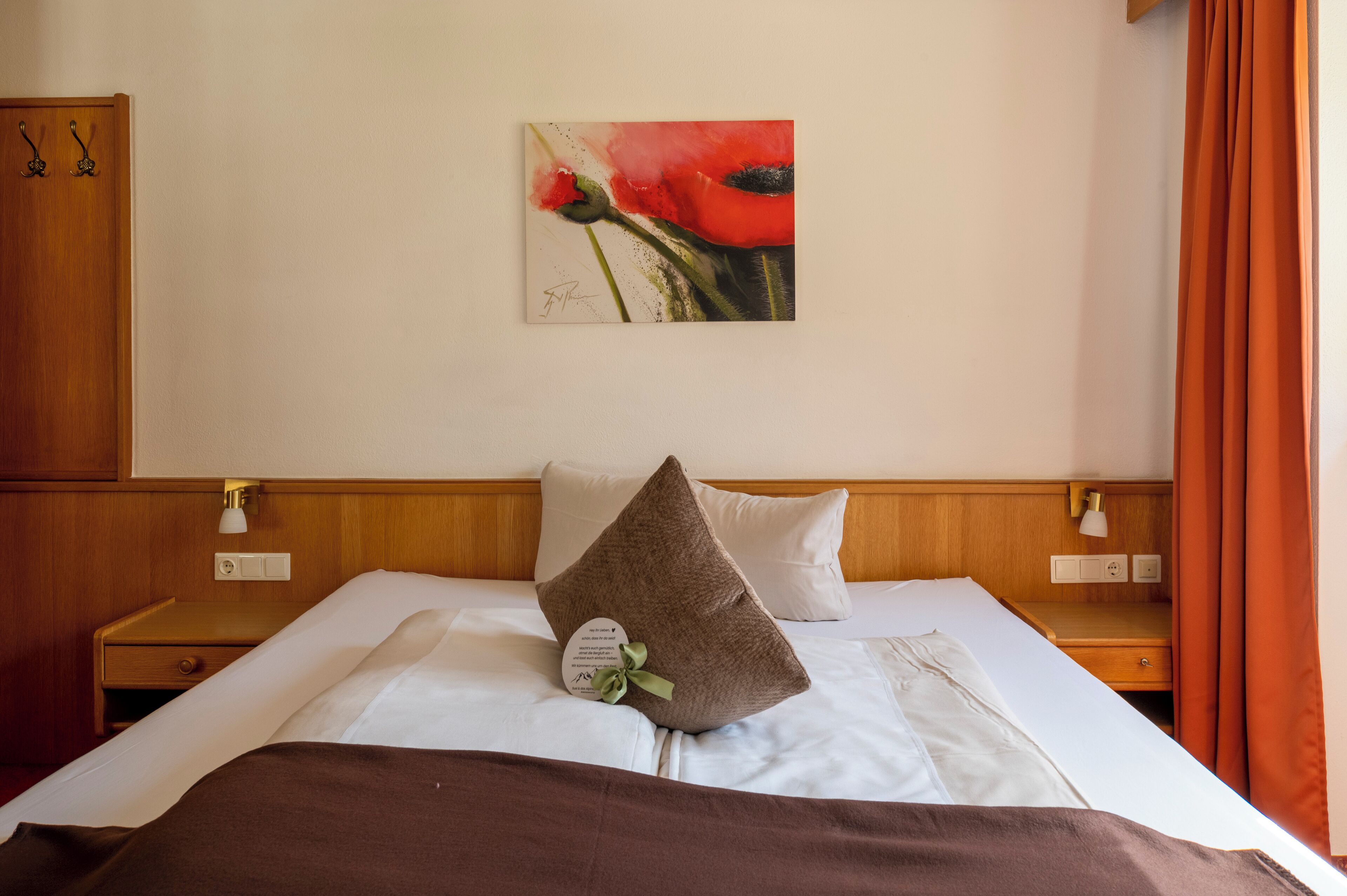 A hotel room with a bed, a nightstand, a lamp, a painting, and a wardrobe.