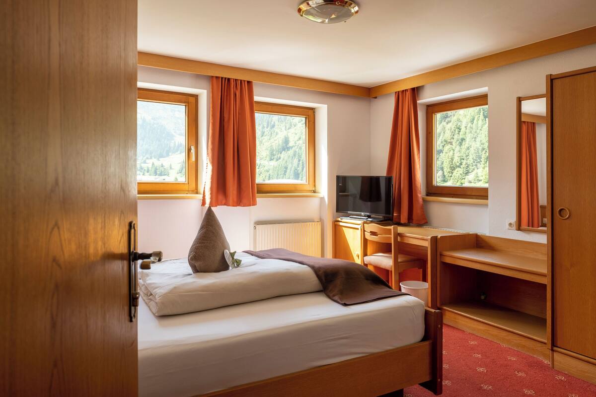A bedroom with a bed, a desk, a TV, and a wardrobe.
