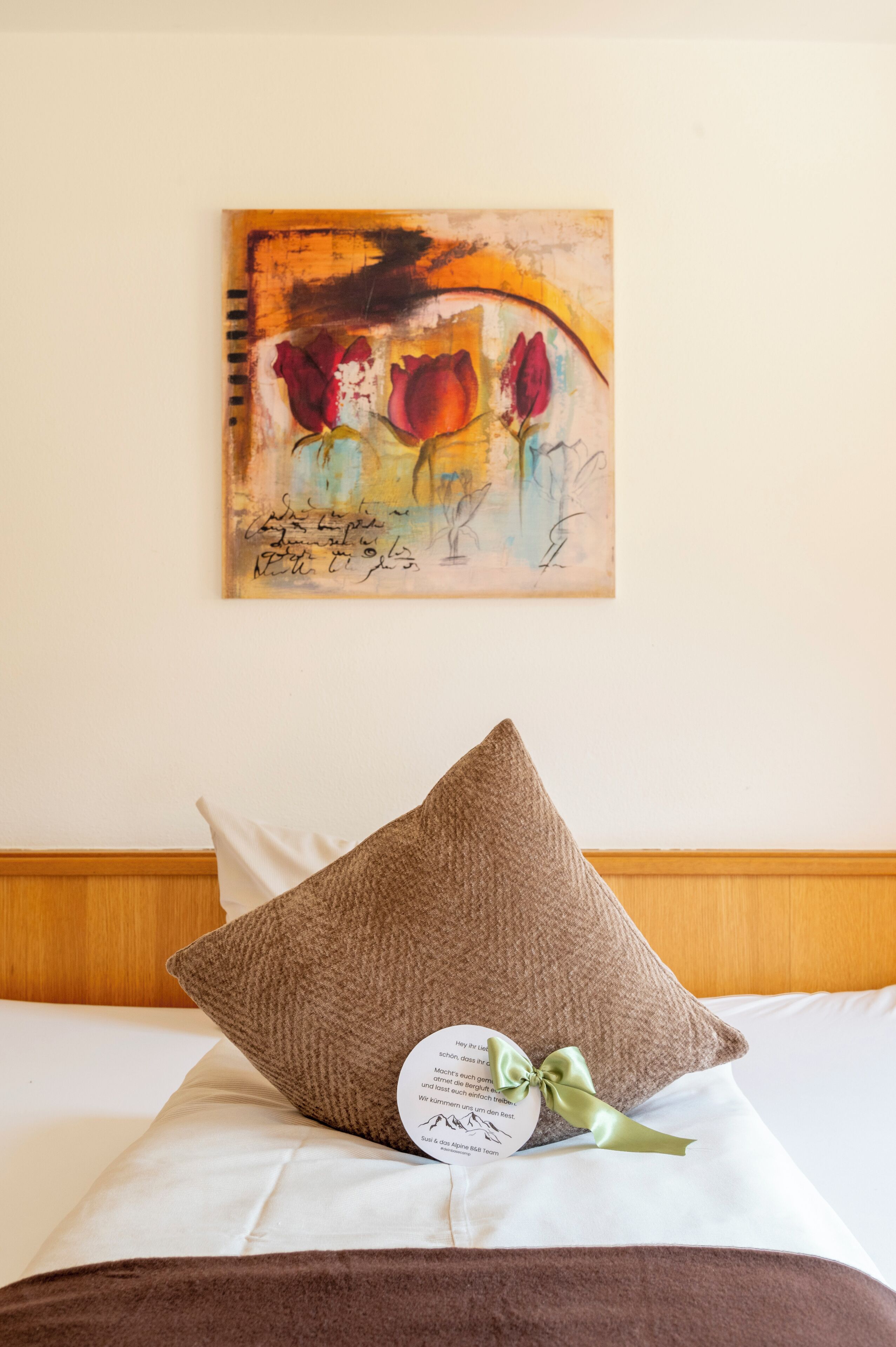 Ein Hotelzimmer mit einem Bett, einem braunen Kopfkissen, einem Zierkissen mit Schleife und einem Bild an der Wand.